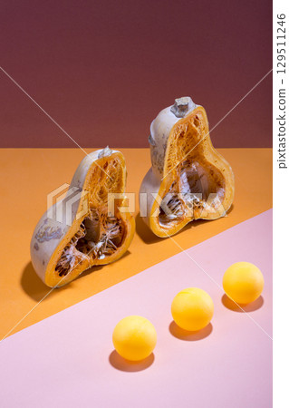 Abstract still life with a cut pumpkin and balls on a multi-colored background Abstract still life with a cut pumpkin and balls on a multi-colored background 129511246