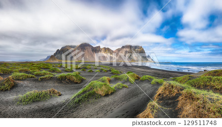 Amazing sunny day and gorgeous rippled black sand beach with dunes and green grass on Stokksnes cape in Iceland. Amazing sunny day and gorgeous rippled black sand beach with dunes and green grass on Stokksnes cape in Iceland. 129511748
