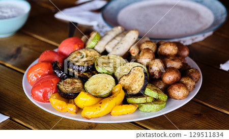Colorful platter of grilled vegetables and sausages served at a rustic outdoor table during a summer gathering Colorful platter of grilled vegetables and sausages served at a rustic outdoor table during a summer gathering 129511834