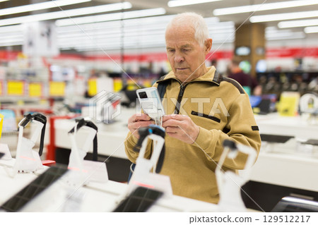 elderly man examines tablet computer in showroom of electronics store 129512217