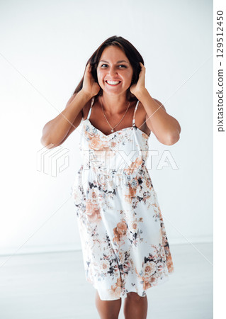 Tanned brunette woman in white summer dress holding her hair with her hands and smiling Tanned brunette woman in white summer dress holding her hair with her hands and smiling 129512450