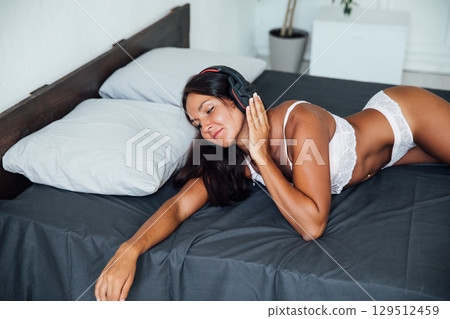 Brunette in lingerie listening to music in headphones and dancing in bedroom Brunette in lingerie listening to music in headphones and dancing in bedroom 129512459