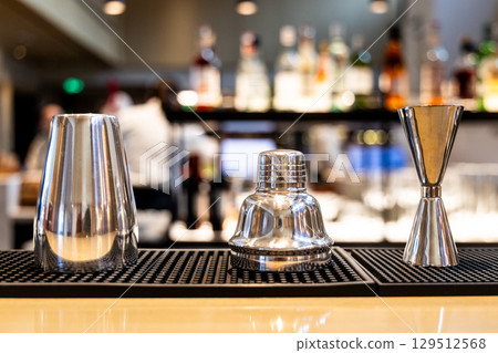 A set of shinny stainless steel barware consisting liquor mixer and jigger with bar background A set of shinny stainless steel barware consisting liquor mixer and jigger with bar background 129512568