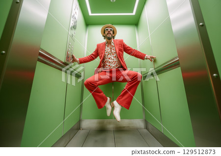 A man in a red suit is jumping in an elevator 129512873