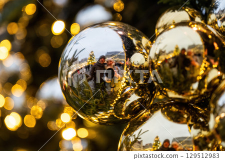 Reflection of couple in golden Christmas bauble with festive lights in background 129512983