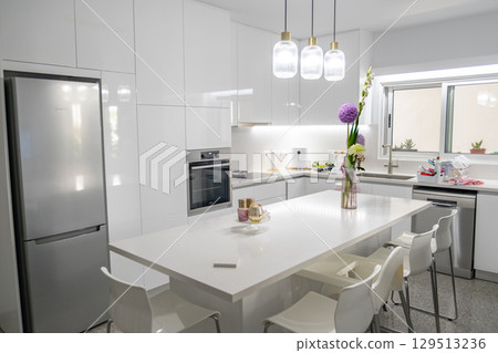 Sleek White Kitchen with Island, Pendant Lights, and Floral Decor Sleek White Kitchen with Island, Pendant Lights, and Floral Decor 129513236