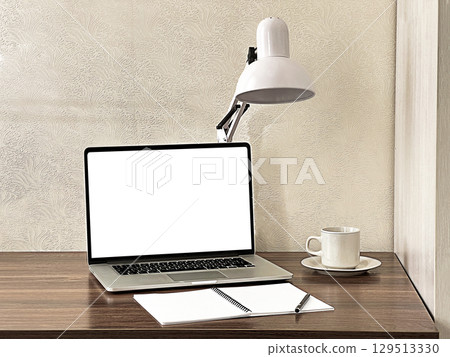 A modern workspace featuring a laptop, a desk lamp, a cup of coffee, and notepads.  129513330