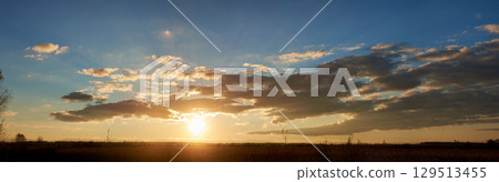 Sun sets low on horizon, casting golden glow across landscape. Fluffy clouds, illuminated with warm hues, float against clear blue sky. Serene scene tranquil, with last light of day fading gently. Sun sets low on horizon, casting golden glow across landscape. Fluffy clouds, illuminated with warm hues, float against clear blue sky. Serene scene tranquil, with last light of day fading gently. 129513455