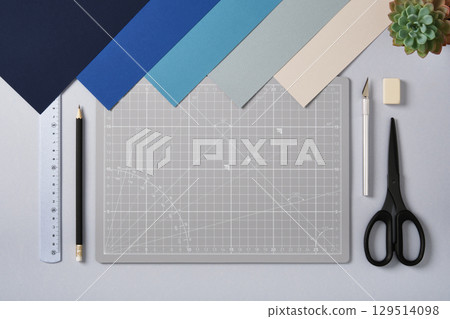 Craft tools, colored paper, and cutting mat arranged neatly on a desk. Creative workspace and design preparation. Copyspace. 129514098