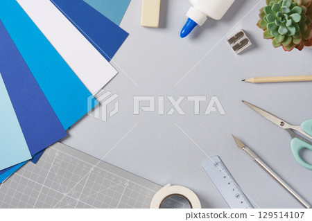 Items for paper crafts in blue and gray colors. Pencil, glue, eraser, knife, scissors and colored pieces of paper. Items for paper crafts in blue and gray colors. Pencil, glue, eraser, knife, scissors and colored pieces of paper. 129514107