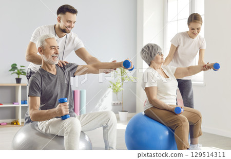 Happy senior man and woman are doing physiotherapy exercises with sports equipment 129514311