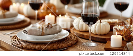 Charming autumn table arrangement features pumpkins, soft lighting, and wine glasses, creating a warm atmosphere perfect for gathering 129514844