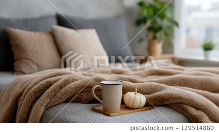 A warm bedroom features soft pillows and a cozy blanket, complemented by a mug of hot cocoa, perfect for autumn relaxation 129514880