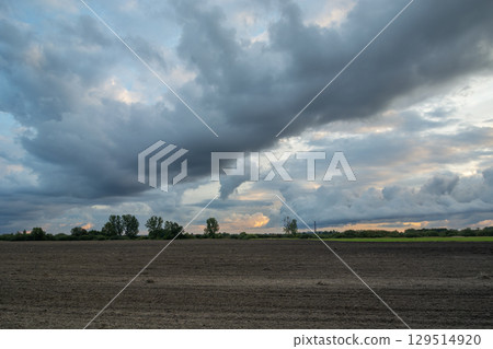 Landscape with evening clouds over a plowed field Landscape with evening clouds over a plowed field 129514920