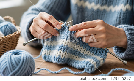 Close-up of hands knitting blue and white striped wool fabric with metal needles at a wooden table Close-up of hands knitting blue and white striped wool fabric with metal needles at a wooden table 129515297