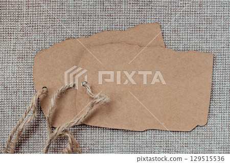 Two kraft paper tags with twine on rustic fabric canvas background, gifts or handmade products. Concept of eco label, artisanal packaging, organic branding, vintage style Two kraft paper tags with twine on rustic fabric canvas background, gifts or handmade products. Concept of eco label, artisanal packaging, organic branding, vintage style 129515536