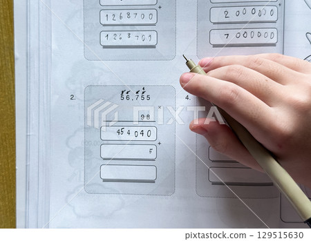 A young student sits at a wooden desk working on basic math exercises, steadily developing essential problem solving skills. 129515630