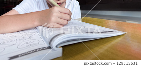 A young student sits at a wooden desk working on basic math exercises, steadily developing essential problem solving skills. 129515631