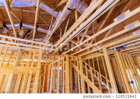 Workers are framing new building, showcasing wooden structure visible ductwork overhead during works day. 129515641