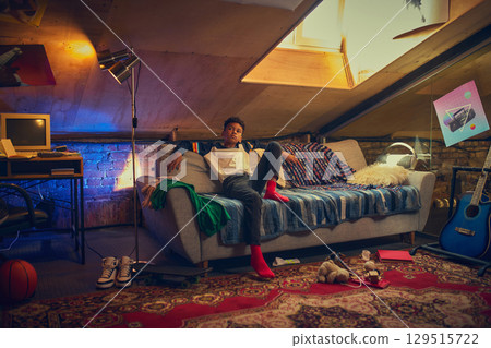 Teen boy relaxing on couch in attic room 129515722