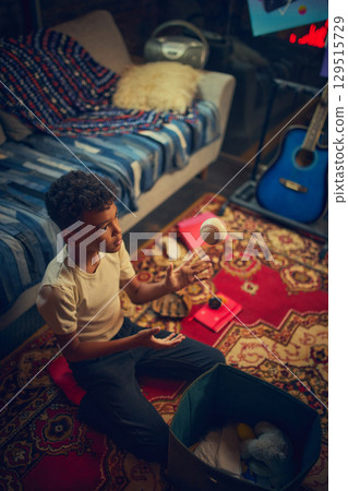 Boy tossing baseball indoors with focused gaze. 129515729