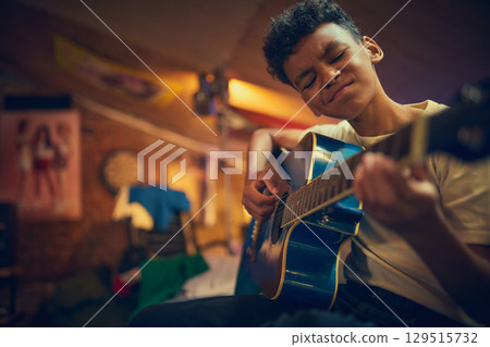 Boy playing guitar with intense facial expression in cozy attic room 129515732