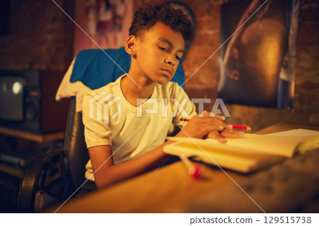 Focused boy writing in notebook at retro desk 129515738
