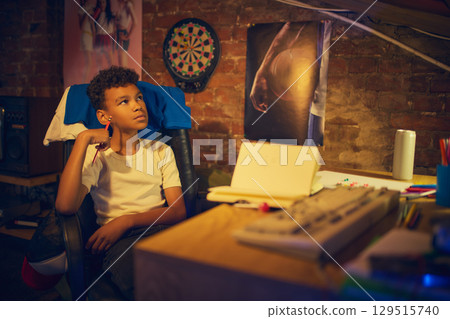 Thoughtful boy holding pencil while sitting at desk 129515740
