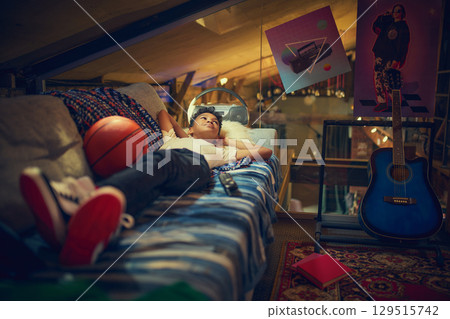Boy daydreaming on sofa in vintage attic with basketball 129515742