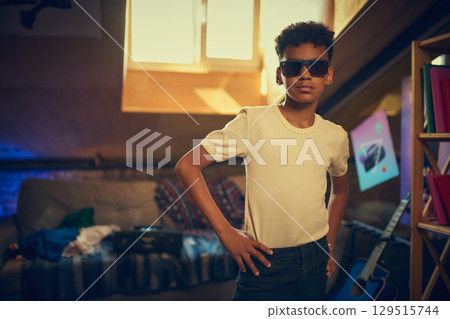 Confident boy posing in sunglasses in retro attic room 129515744