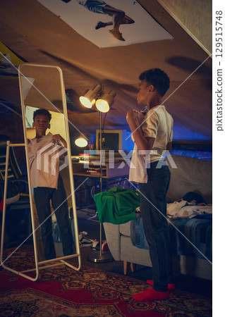 Teen choosing outfit in front of mirror in retro loft 129515748