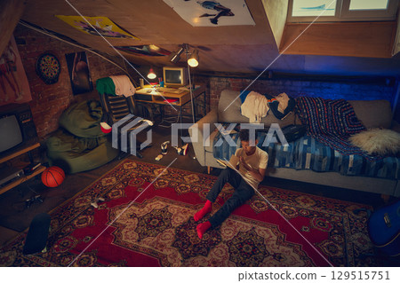 Boy writing notes in cozy attic with 90s retro vibe 129515751