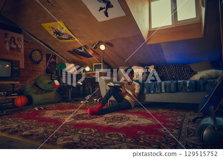Teen boy reading notebook in retro attic bedroom 129515752