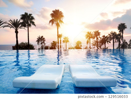 Serene Sunset by the Infinity Pool Beautifully Surrounded by tropical Palm Trees Serene Sunset by the Infinity Pool Beautifully Surrounded by tropical Palm Trees 129516033