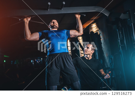 Male bodybuilder performing lat pulldown with personal trainer in gym, Man training back muscles under coach guidance during workout Male bodybuilder performing lat pulldown with personal trainer in gym, Man training back muscles under coach guidance during workout 129516273