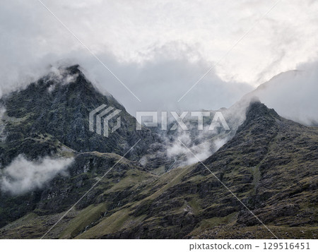 The image focuses on a mountain slope. Its composition primarily consists of rock and sporadic plant life, with small waterfalls. Clouds are in the top section. The image focuses on a mountain slope. Its composition primarily consists of rock and sporadic plant life, with small waterfalls. Clouds are in the top section. 129516451