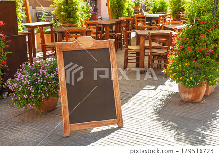 Empty outdoor cafe with blank chalkboard menu sign on a sunny street in Italy Empty outdoor cafe with blank chalkboard menu sign on a sunny street in Italy 129516723