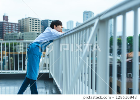 A man wearing an apron resting on the balcony 129516948