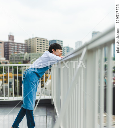 A man wearing an apron looks out from the balcony 129517723