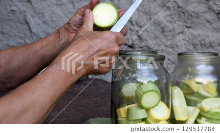 Old woman slices raw zucchini for homemade canning of vegetable preservation Old woman slices raw zucchini for homemade canning of vegetable preservation 129517783