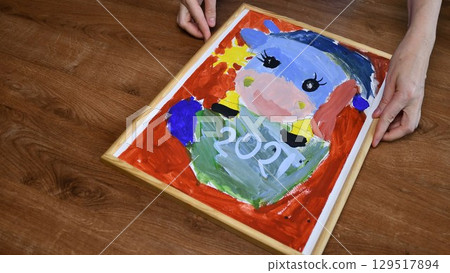 Female hands put wooden picture frame at kids painting 129517894