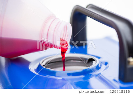 Red oil is added to the fuel, generator with two-stroke engine, close up. Pouring red liquid oil into the open cap of generator, maintenance of the device 129518116