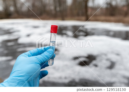 Test tube with water inside in hand of a person, close up. Foam on water surface on the background, checking the pollution level, environmental concept Test tube with water inside in hand of a person, close up. Foam on water surface on the background, checking the pollution level, environmental concept 129518130