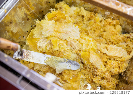 Tank full of wax caps after uncapping honey frames for harvest. Wax and electric knife for uncapping frames, harvest of honey on apiary 129518177