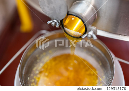 Ripe harvested honey floating from honey extractor through the double cleaning filter. Harvest of honey using professional beekeeping equipment, fresh summer honey 129518178