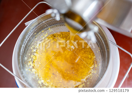 Top down view of honey floating from extractor machine to bucket through cleaning filter. Harvest of honey on the apiary, cleaning honey from parts of wax caps 129518179