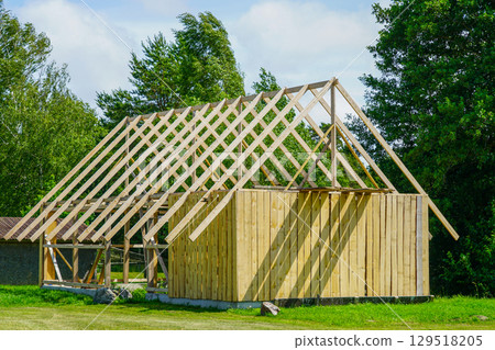 Wooden House Frame Construction with Roof Trusses in Rural Outdoor Setting Wooden House Frame Construction with Roof Trusses in Rural Outdoor Setting 129518205