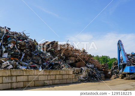 Scrap metal recycling yard with blue crane and large piles of sorted ferrous and non-ferrous waste 129518225