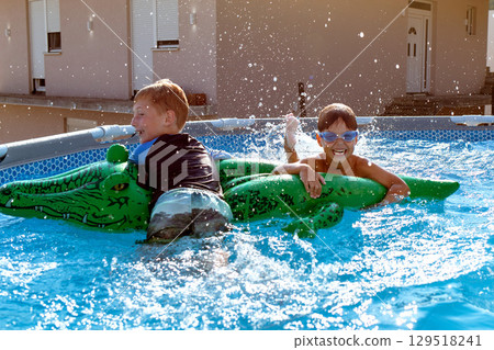 Two boys playing on inflatable crocodile in swimming pool 129518241