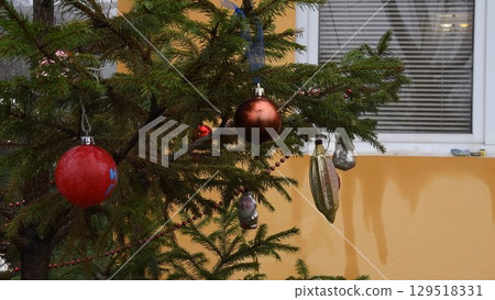 Vintage baubles and red Christmas balls on Christmas tree at backyard of yellow house 129518331